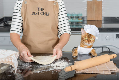 The owner woman and her cat are having fun preparing a pie or pizza in the kitchen together.