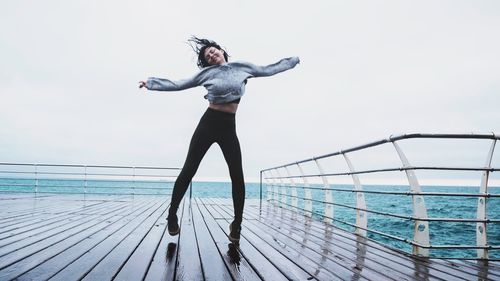 Woman jumping over pier at beach against sky