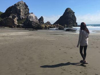 Rear view of woman walking on beach with rocks in the distance