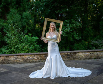 Woman standing against white wall with trees in background