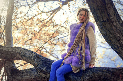 Portrait of smiling young woman standing on tree trunk