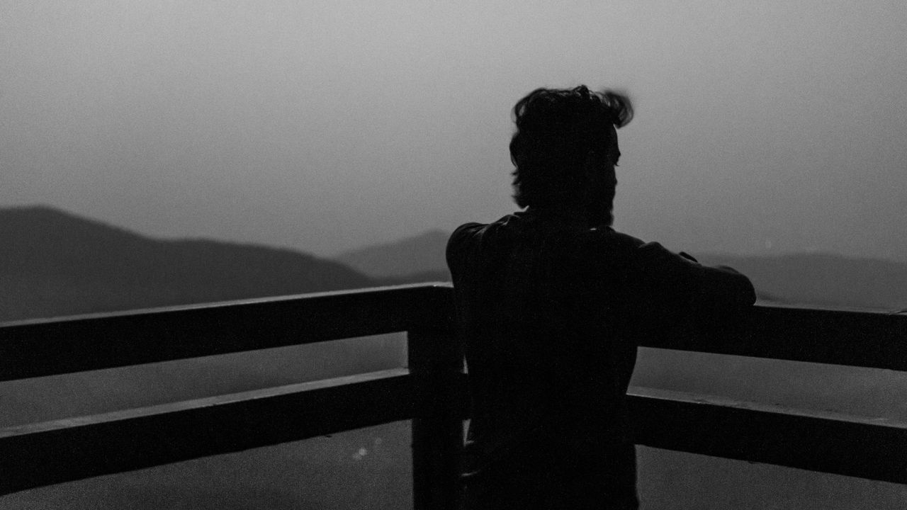 REAR VIEW OF WOMAN STANDING BY RAILING AGAINST SKY