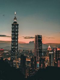 Illuminated buildings in city against sky during sunset