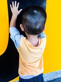 Rear view of boy standing against yellow