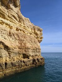 Rock formation by sea against blue sky