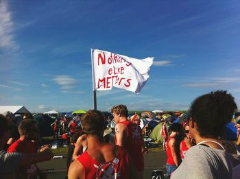 People standing on street by flag with text against sky