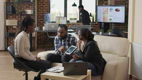 Businessman discussing with colleague sitting on sofa in office