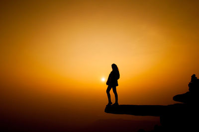 Silhouette woman standing on cliff against sky during sunset