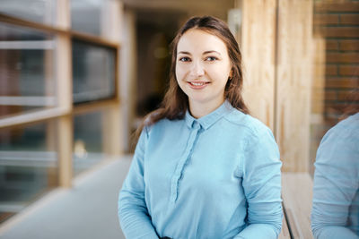 Portrait of happy young businesswoman standing at office corridor