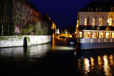 Illuminated buildings by river against sky at night