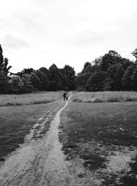 People walking on road amidst field against sky