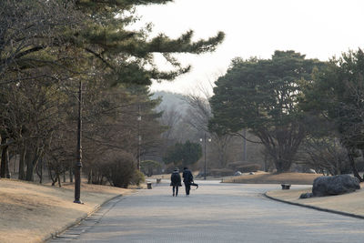 Rear view of people walking on road amidst field