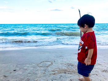 Boy standing at beach against sky