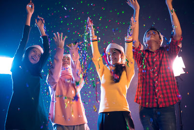 Low angle view of cheerful friends with confetti at night