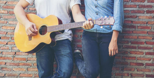 Midsection of man playing guitar with woman against brick wall