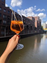 Hand holding glass of water against buildings