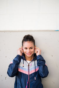 Portrait of young woman listening music through headphones against wall