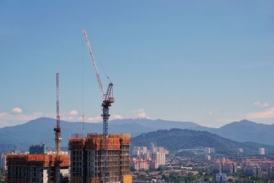 Cranes in city against clear sky