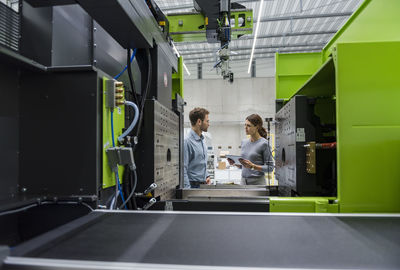 Colleagues in high tech company controlling manufacturing machines, using digital tablet