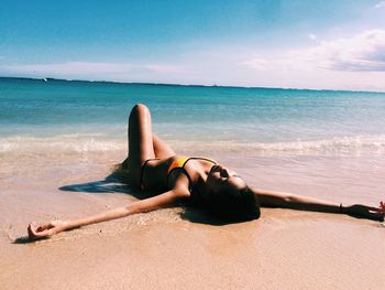 Sensual young woman lying on beach against sky in magic island