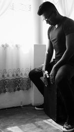 Young man looking away while sitting on wall at home