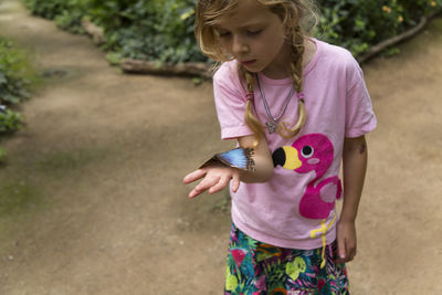 Girl holding butterfly while standing on land