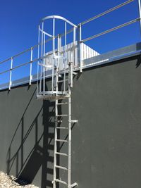 Ladder on surrounding wall against blue sky