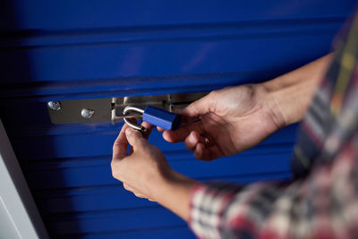 Anonymous cropped woman hands holding a blue padlock while closing it