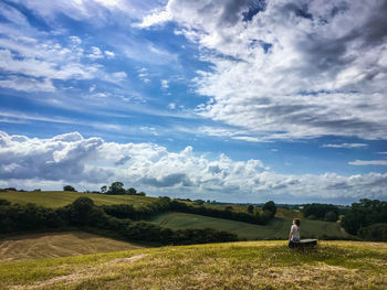 Scenic view of field against sky and a girl on a bench