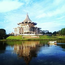 View of temple by lake against cloudy sky