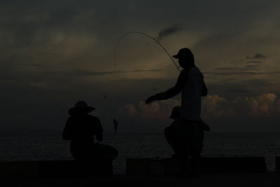 Silhouette man fishing at beach against sky during sunset