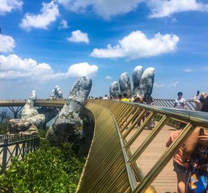 People at footbridge against cloudy sky