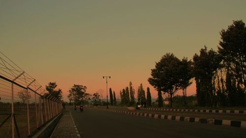 Road amidst trees against clear sky during sunset