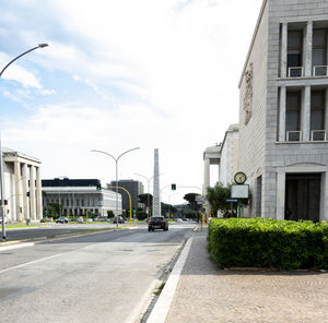 Road by buildings in city against sky