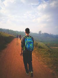 Rear view of man walking on landscape against sky