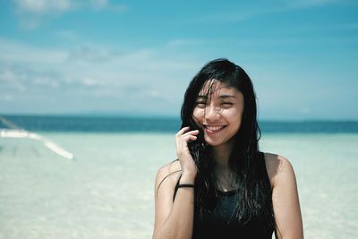 Smiling young woman standing at beach against sky