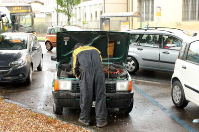 Rear view of man repairing car on street during rainy season