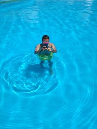 High angle view of young man using mobile phone in swimming pool during sunny day