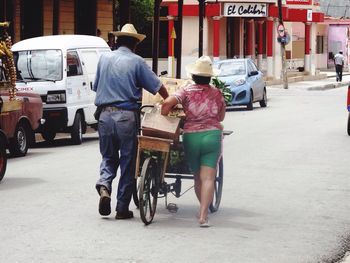 Rear view of man and woman with push carts walking on street