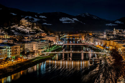 Illuminated buildings by lake against sky in city at night