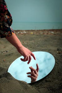 My hand on beach against sky