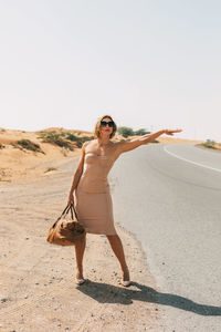 A stylish woman catches a car on a deserted road on a sunny day