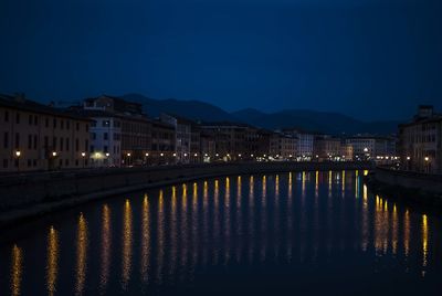 Illuminated buildings by lake against sky at night