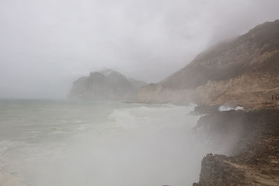 Waves splashing on rock formation against sky