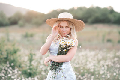 Beautiful woman holding flowers standing on field