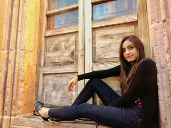 Low angle portrait of stylish woman sitting on wooden window sill