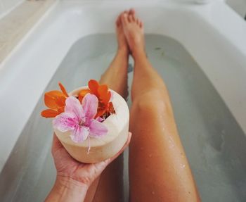 Low section of woman holding flowers in bathtub