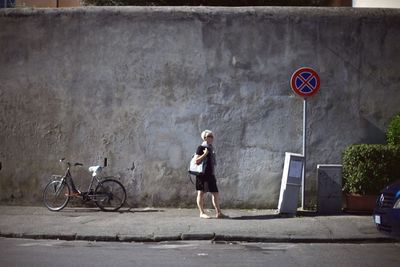 Woman standing by bicycle on footpath against retaining wall