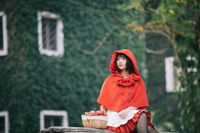 Woman with red umbrella sitting against trees