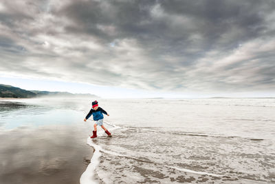 Child running in water at new zealand beach on cloudy afternoon